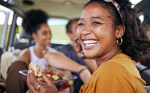Woman smiling while eating lunch with friends on road trip