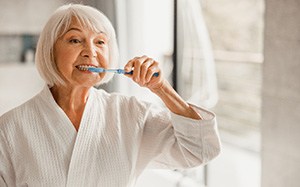 Older woman brushing her teeth in her bathrobe