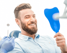 Man in dental chair looking at smile in mirror