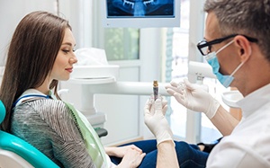 Dentist holding a dental implant model while talking with patient