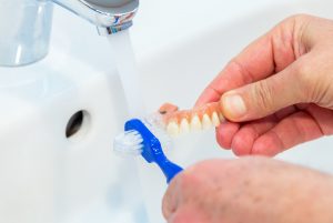 Person cleaning denture in sink