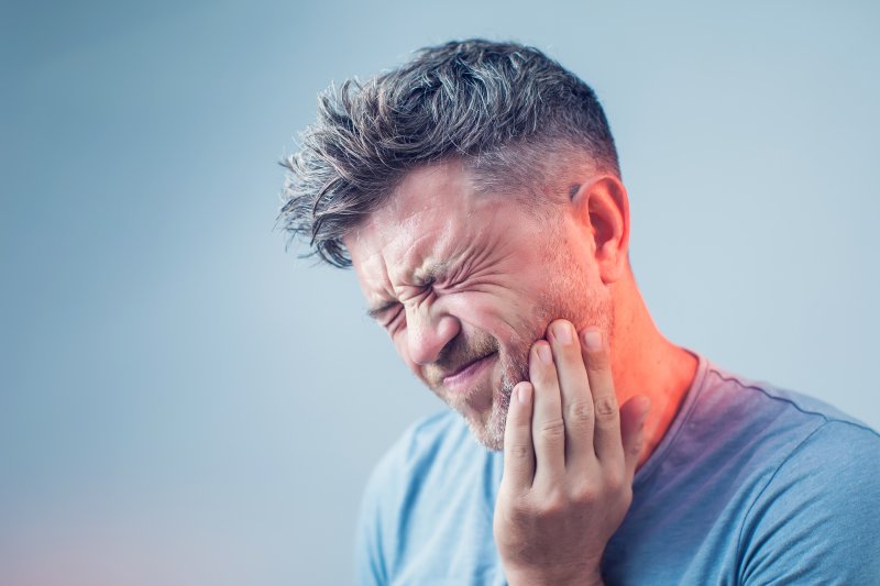 person with dental emergency holding face in pain