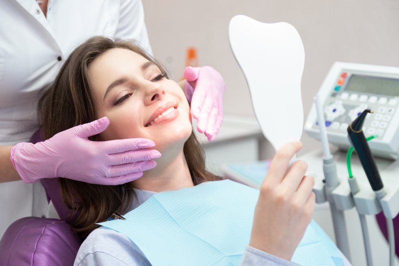 A woman smiling in a mirror after her cosmetic dentist treated her