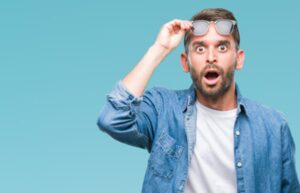 Man with surprised expression lifting sunglasses.